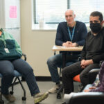 Several people sit at desks in a group talking.